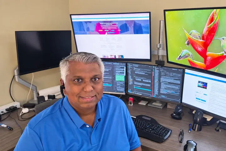 David Ramroop, founder of Promora Solutions, at his desk with websites and code on his monitors